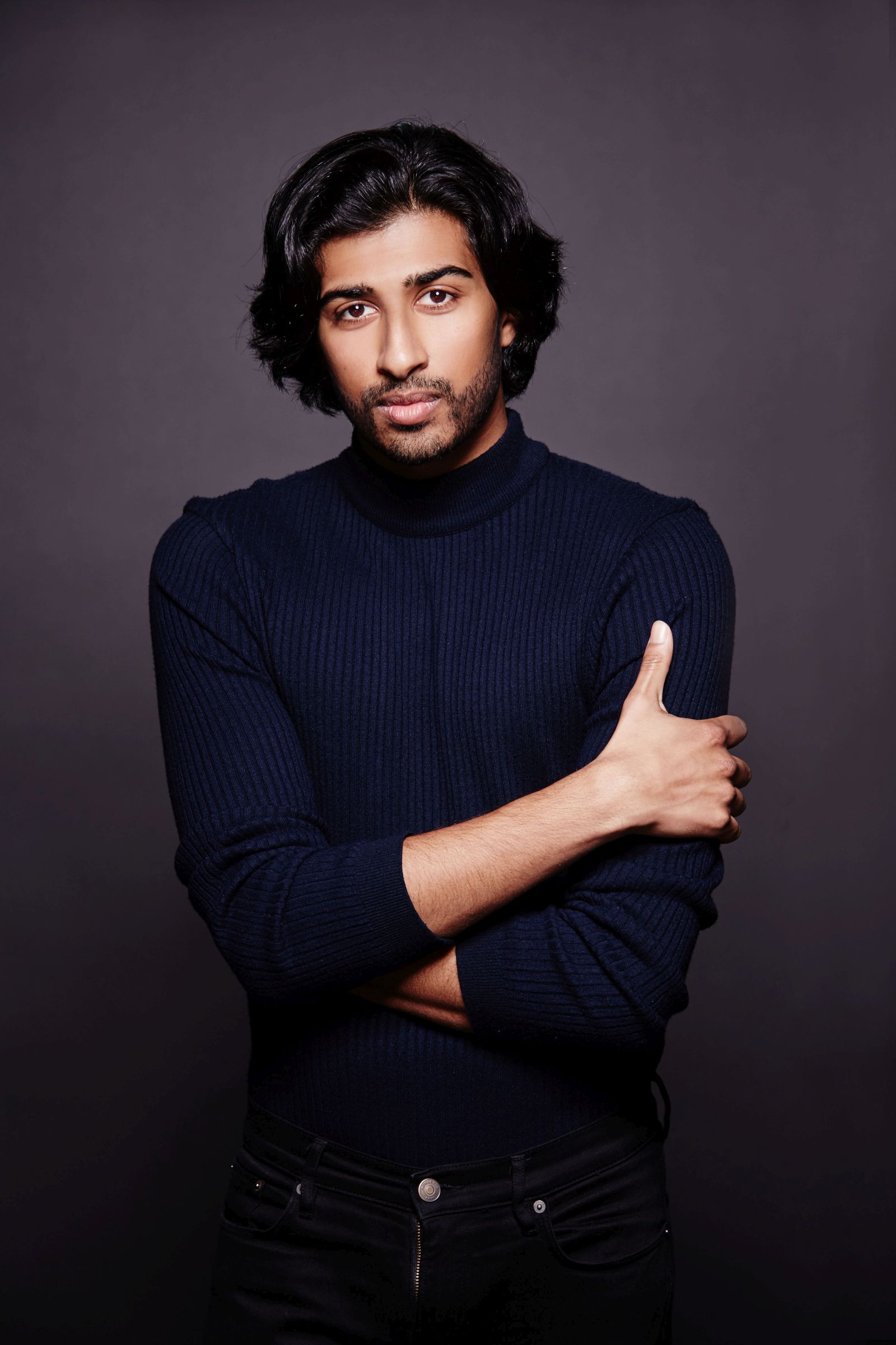Person wearing a dark sweater with arms crossed, against a dark background.