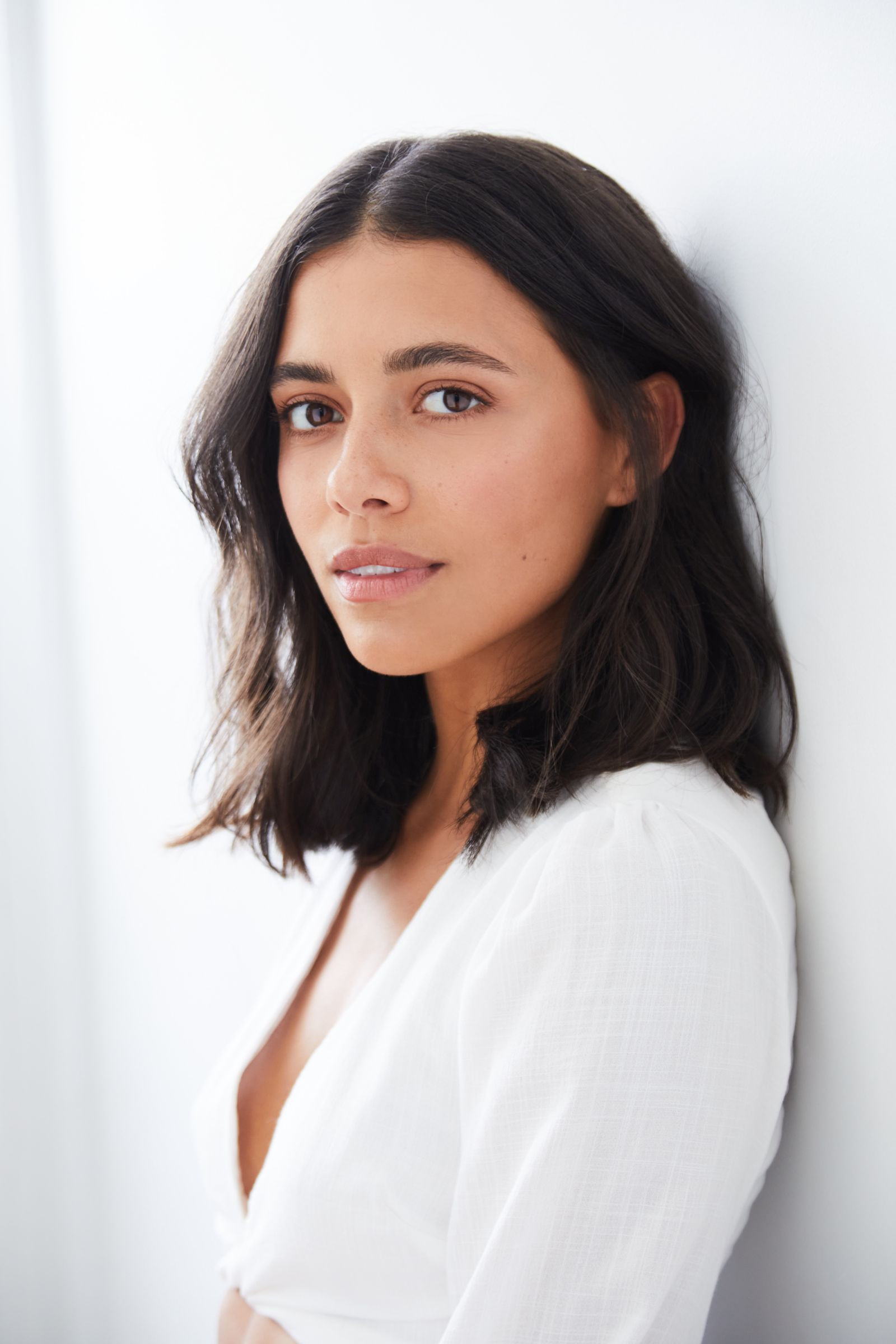 Woman with shoulder-length dark hair in a white top against a light background.