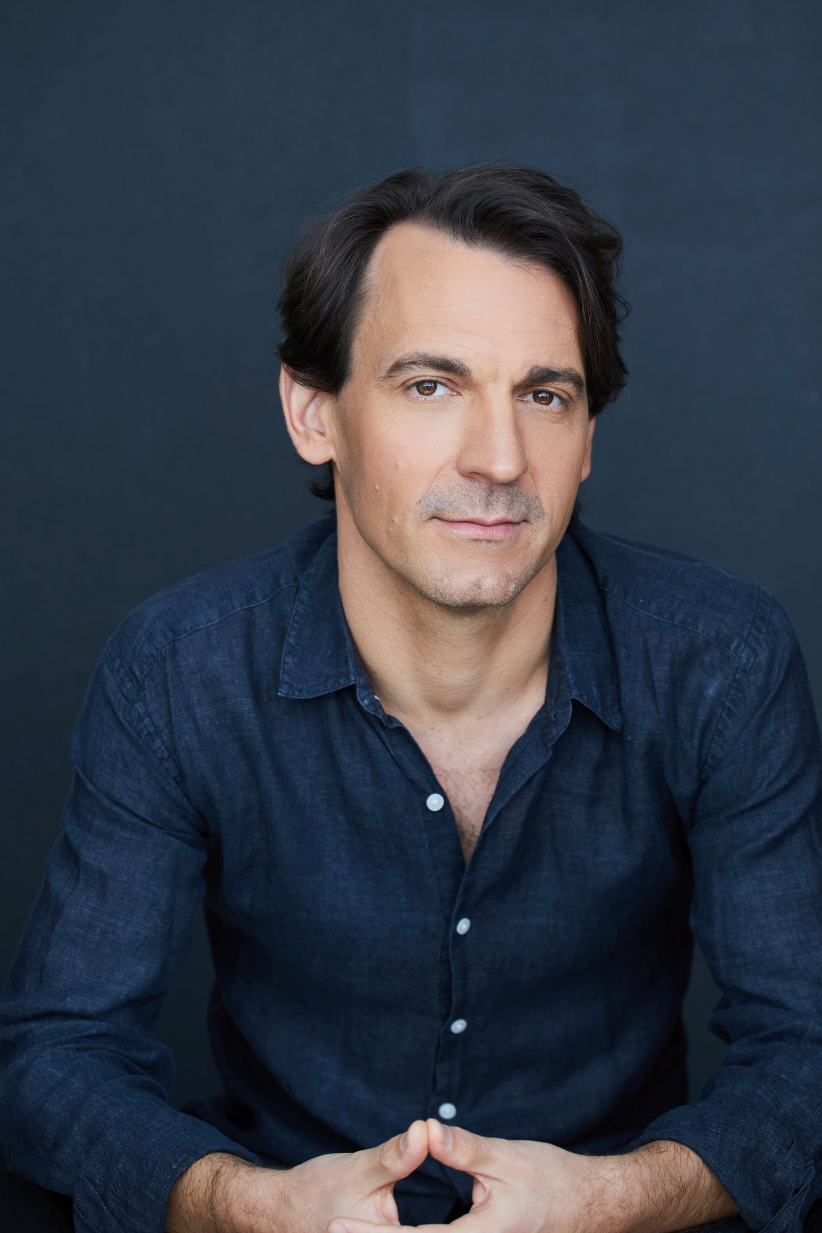 Man in a dark blue shirt with a neutral expression.