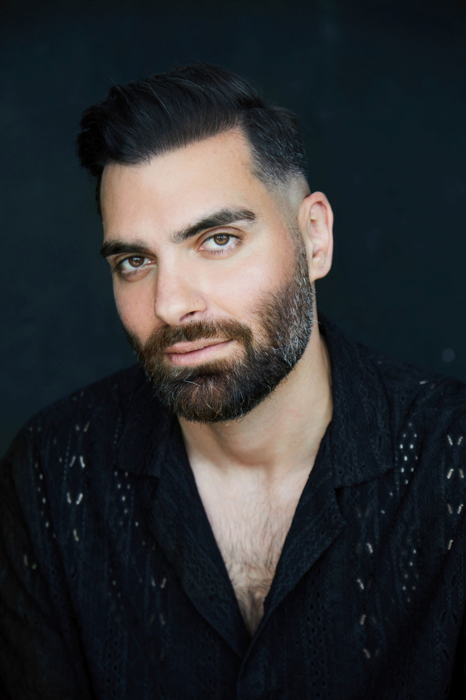 Portrait of a man with a beard and dark hair wearing a patterned shirt.