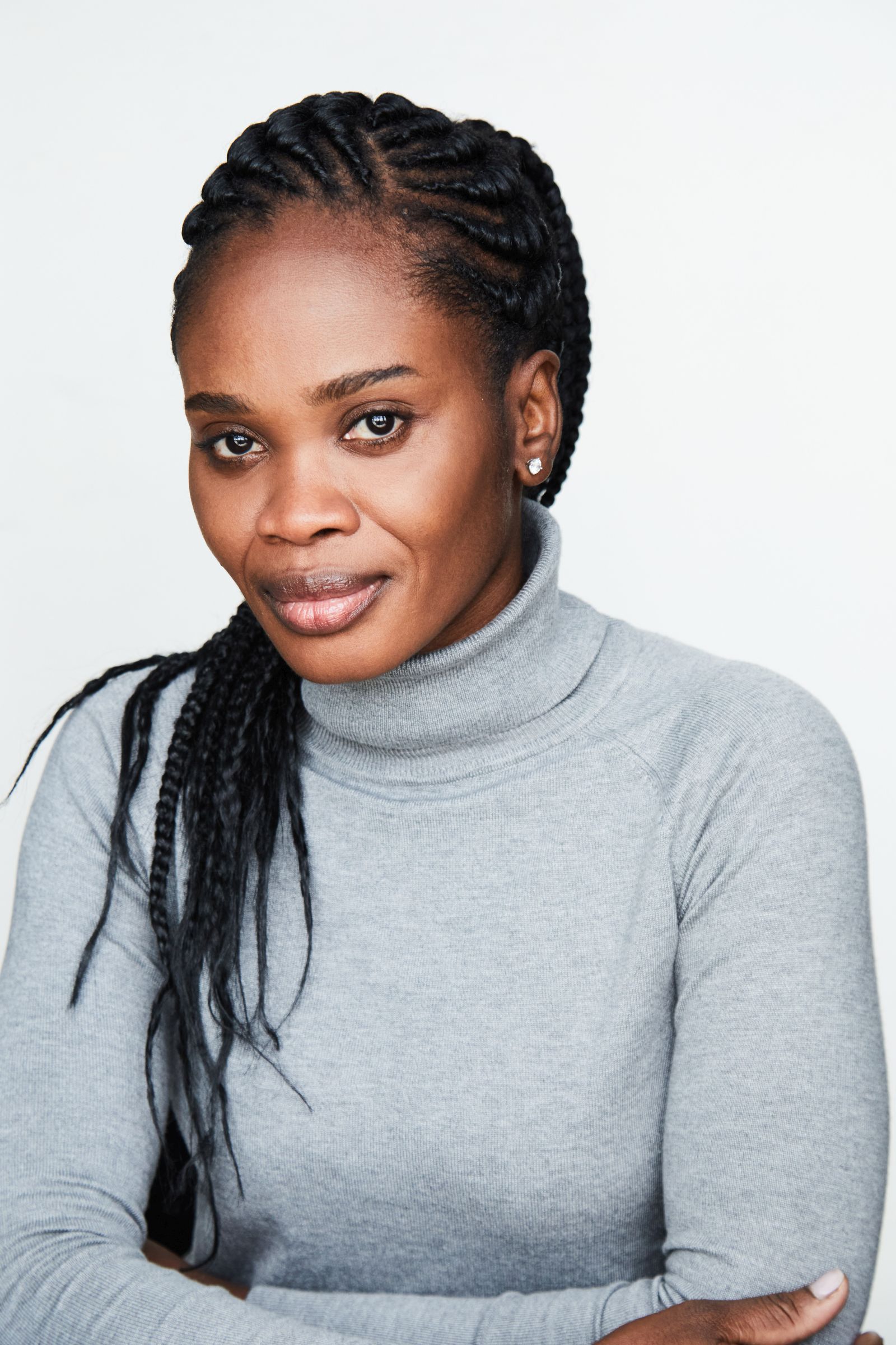 Woman with braided hair in gray turtleneck sweater against white background.