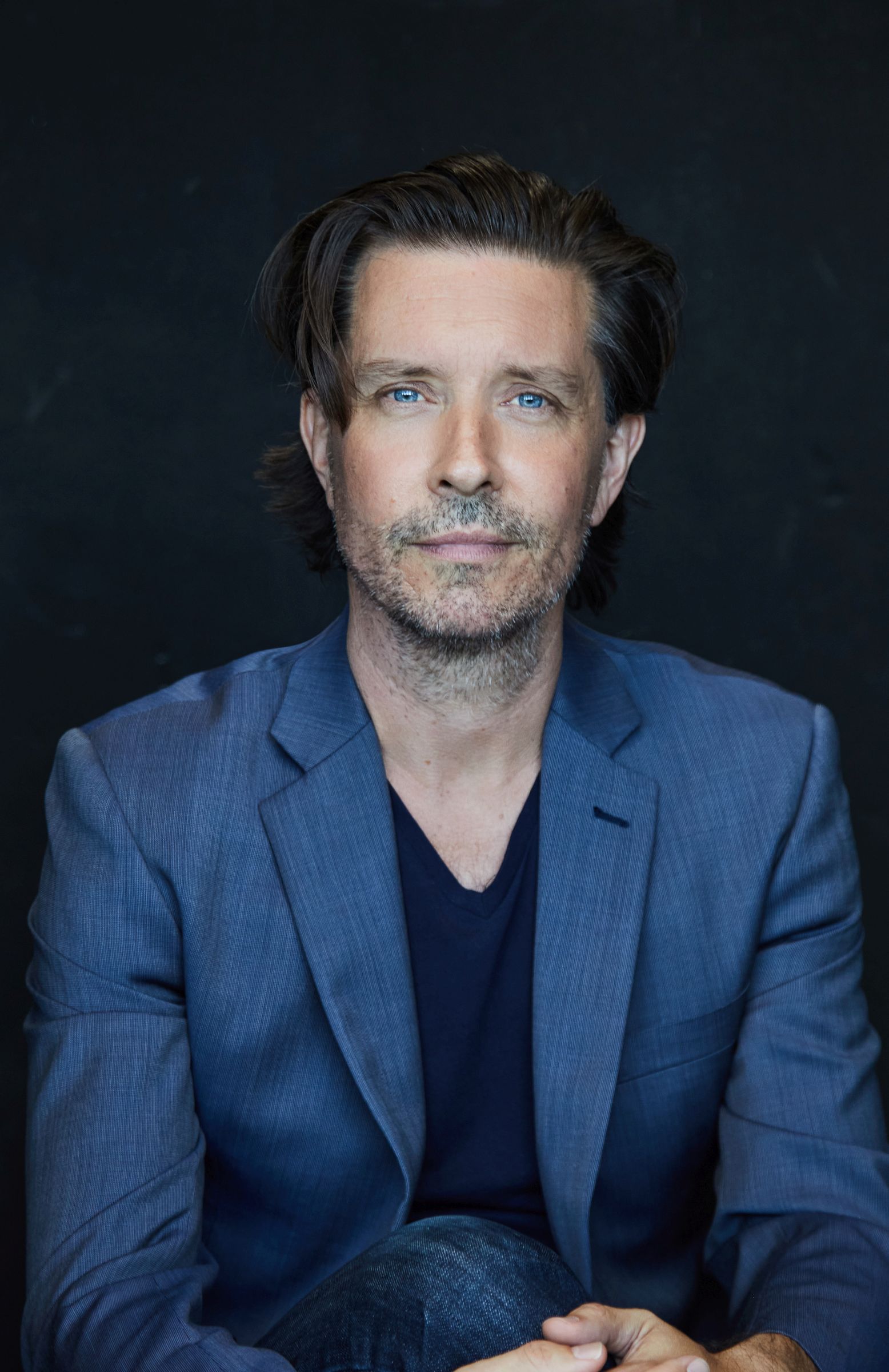 Man in a blue blazer against a dark background.