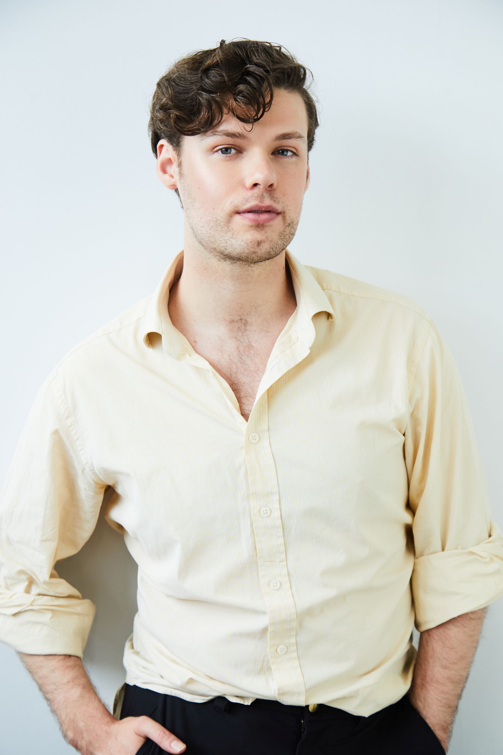 Man with curly hair in a cream shirt against a white wall.