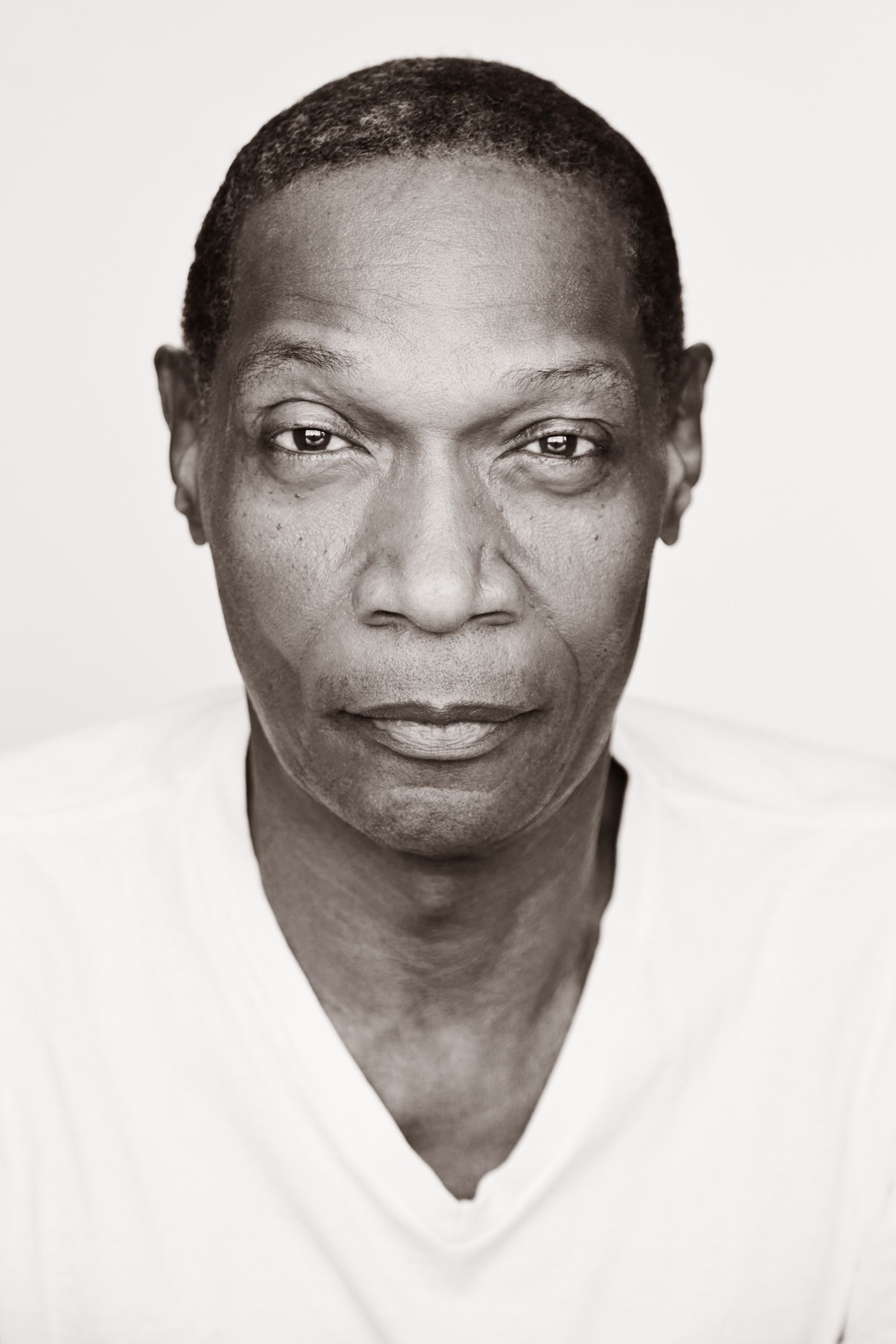 Sepia portrait of a man in a white shirt looking directly at the camera.