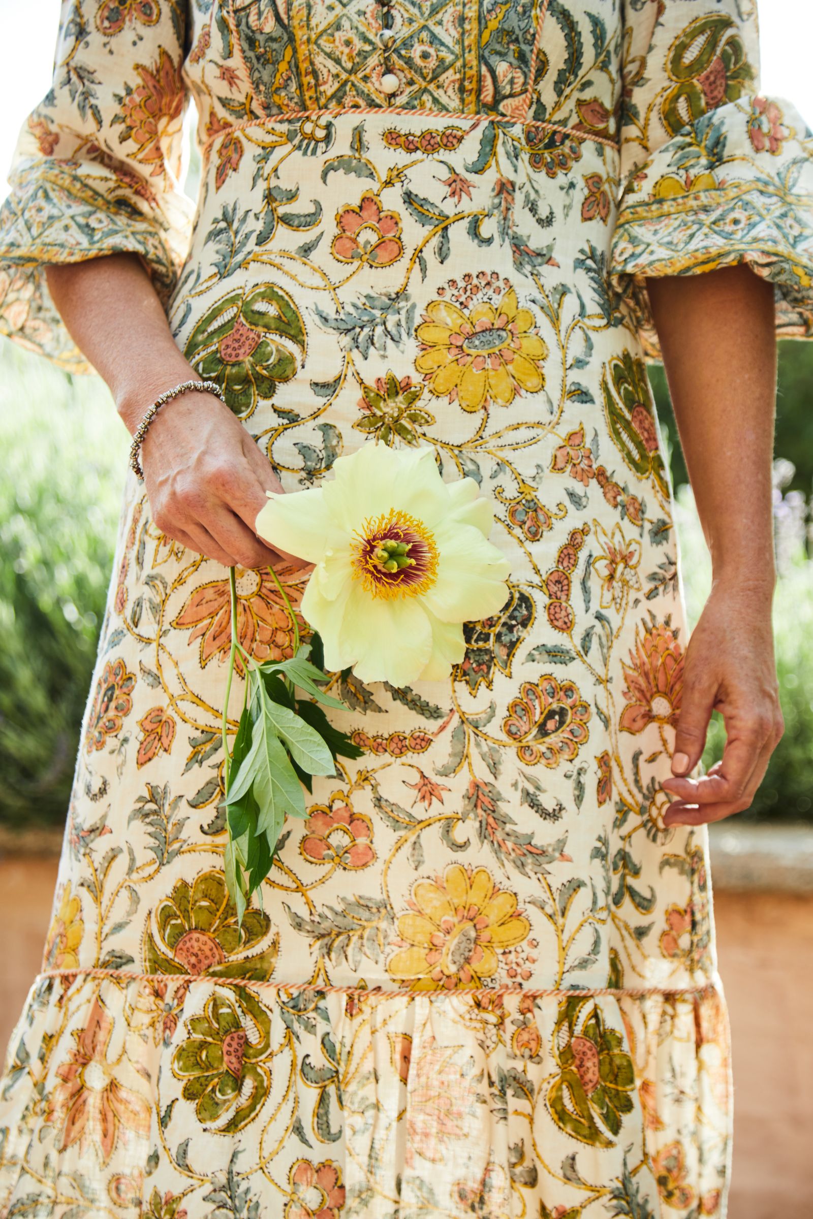Hand holding a pale yellow flower against an ornate patterned dress.