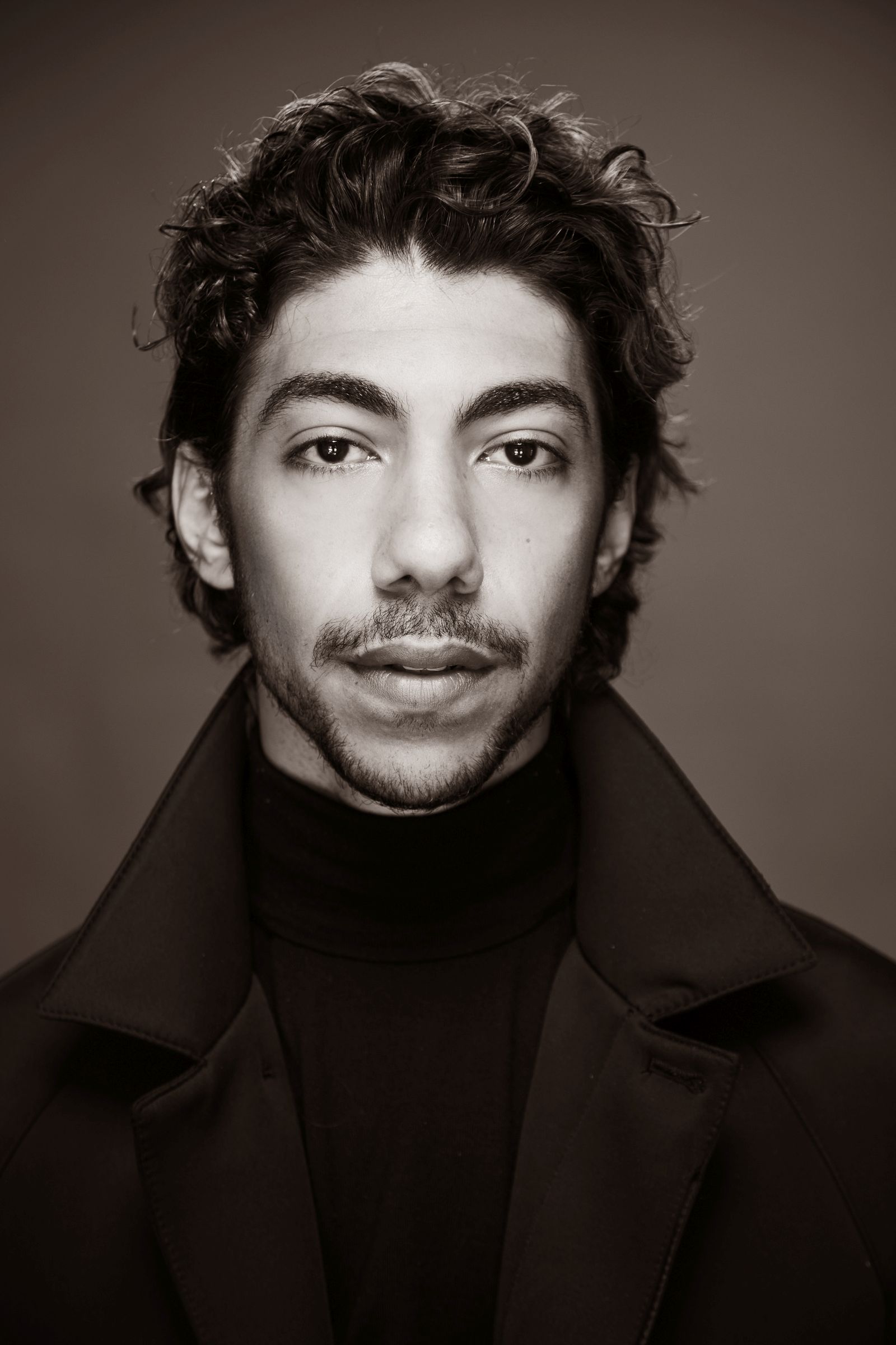 Black and white portrait of a man with curly hair and a dark jacket.