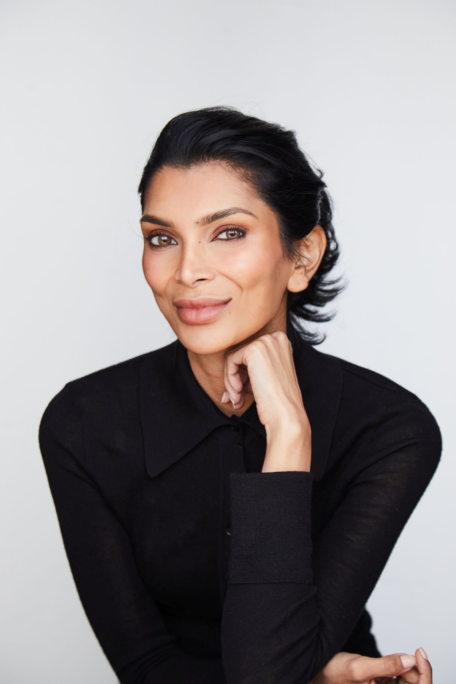 Person with dark hair, in a black top, resting chin on hand.