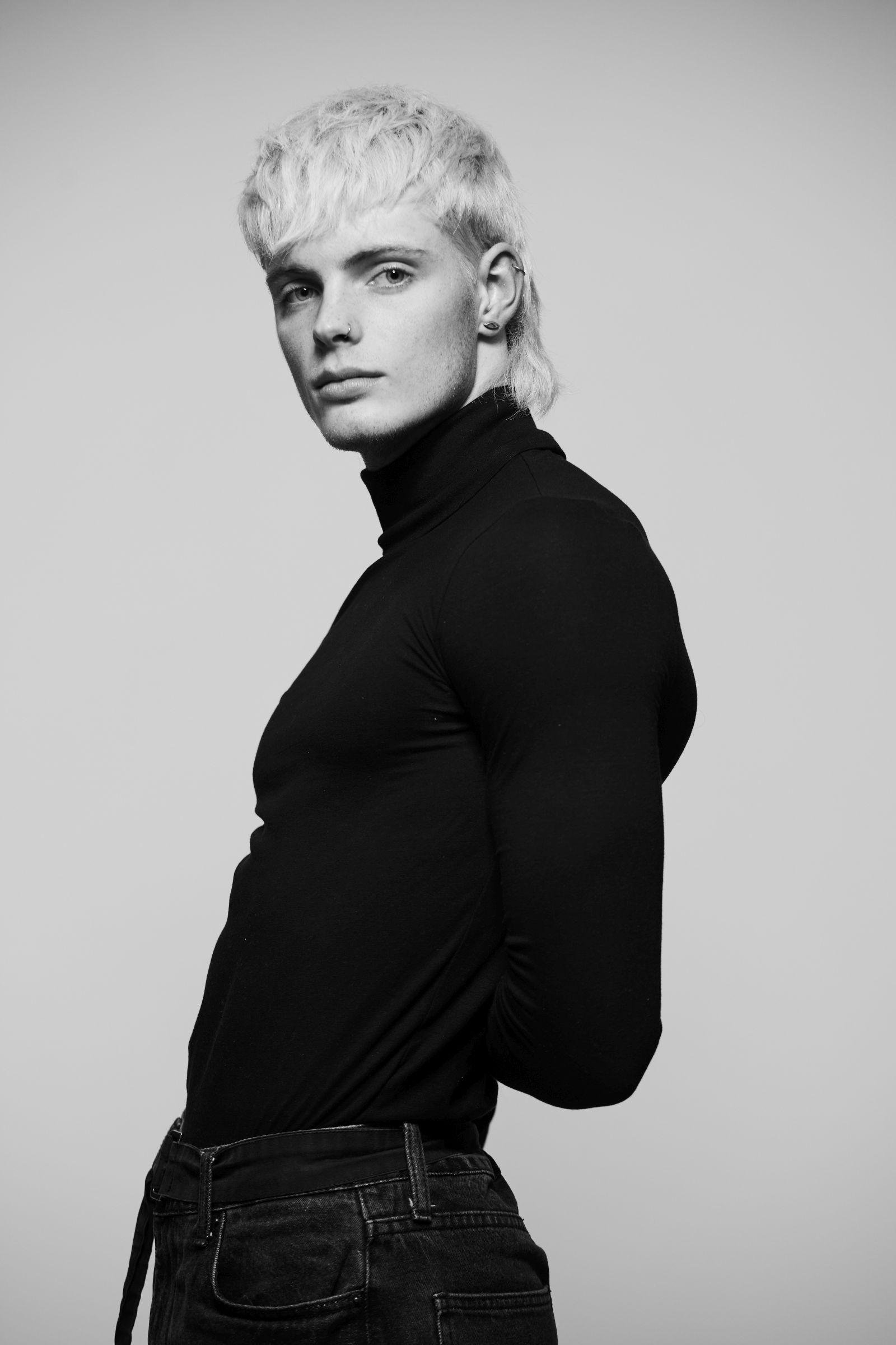 Black-and-white studio portrait of person with platinum mullet, nose ring, black turtleneck.