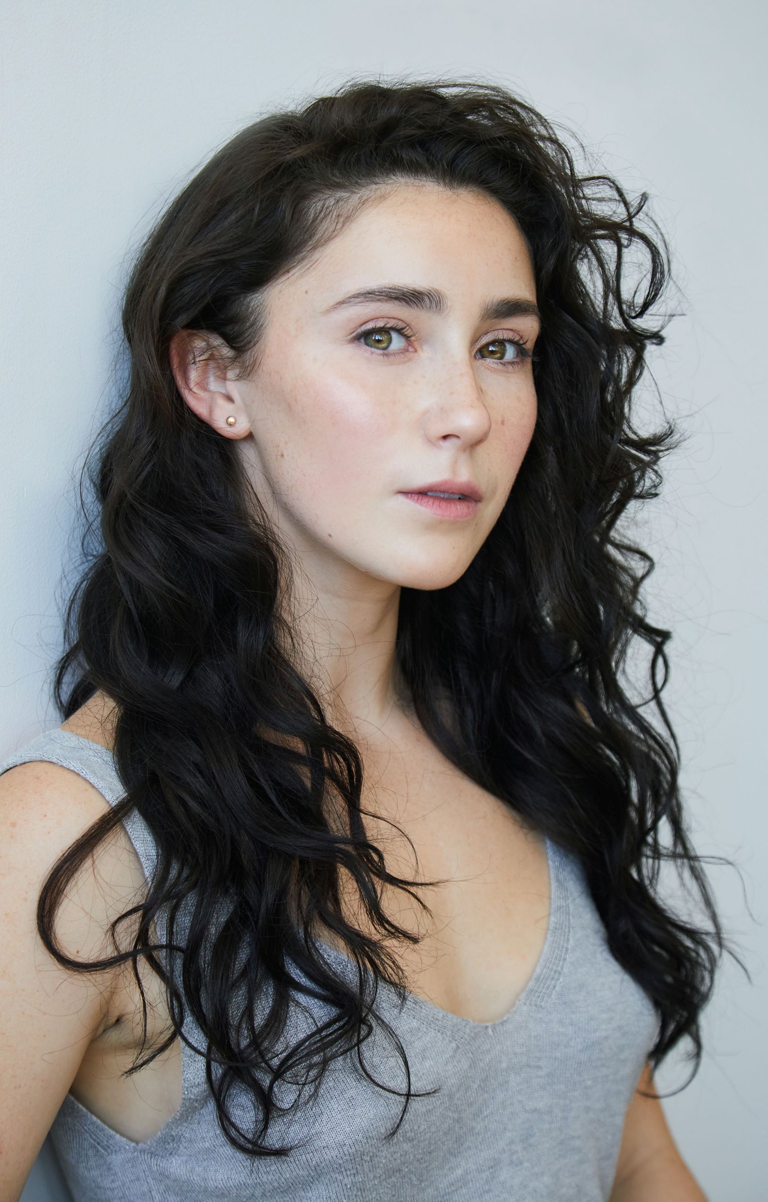 Person with long dark hair and a neutral expression, wearing a gray tank top.