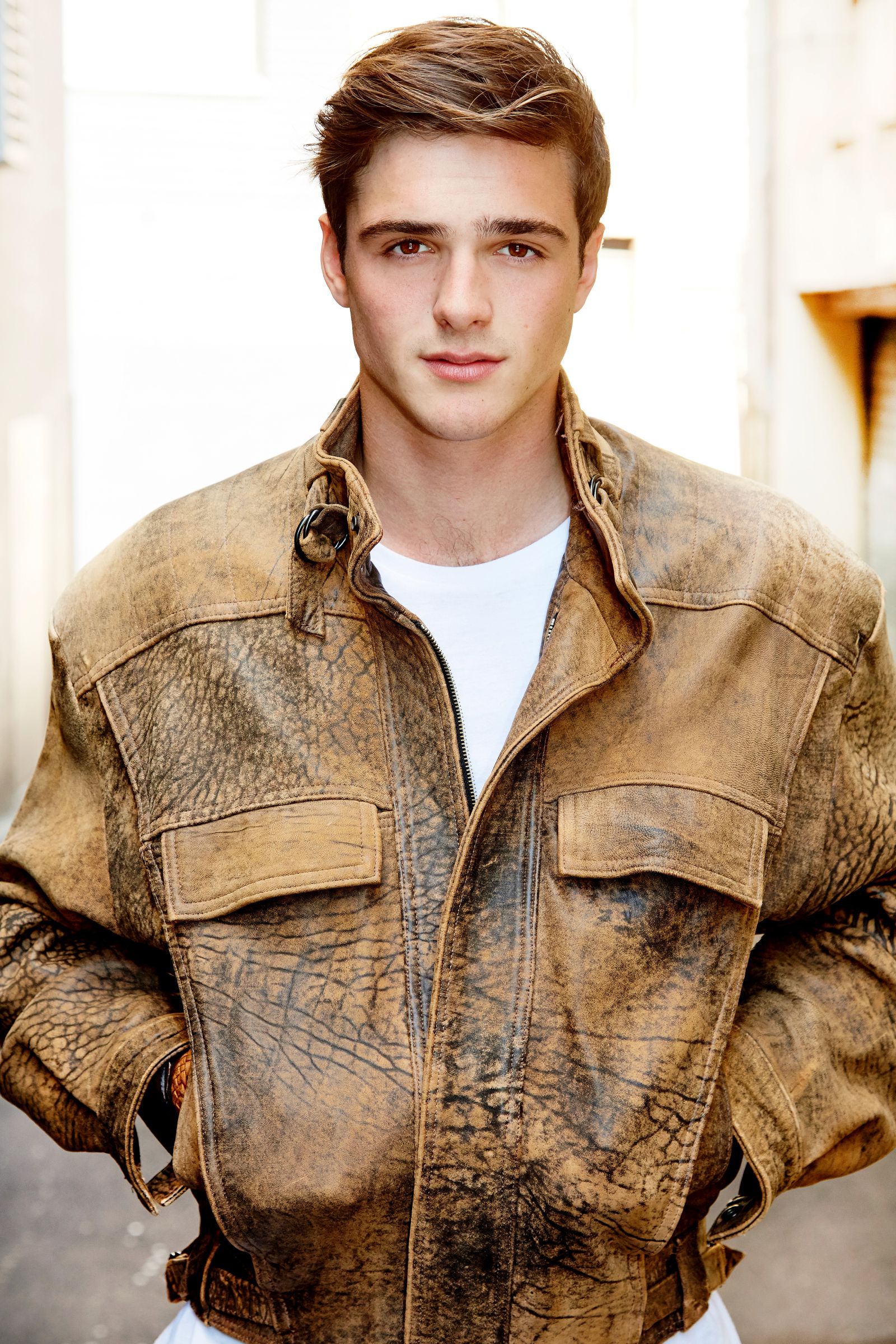 Young man wearing a brown leather jacket in a sunlit alley.