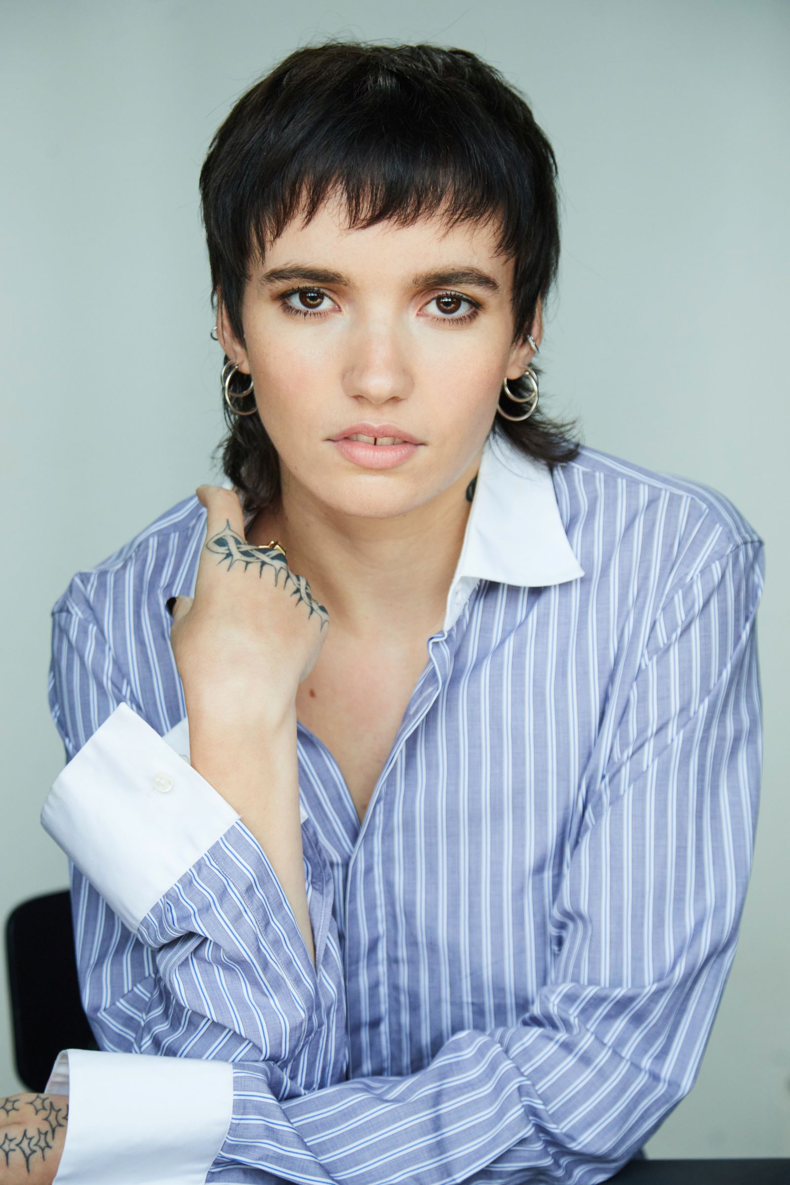 Person with short hair in striped shirt and hand tattoo.