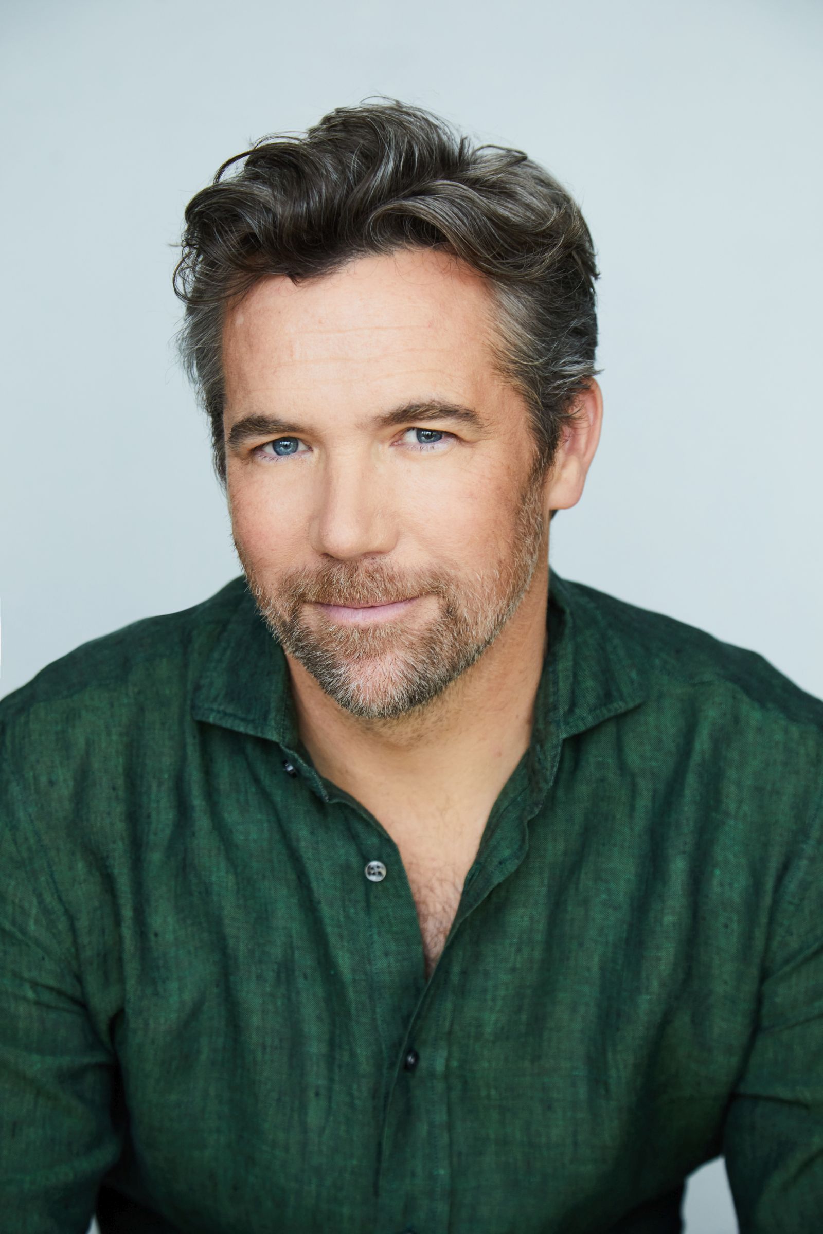 Man with short hair and beard wearing a green shirt, smiling softly.