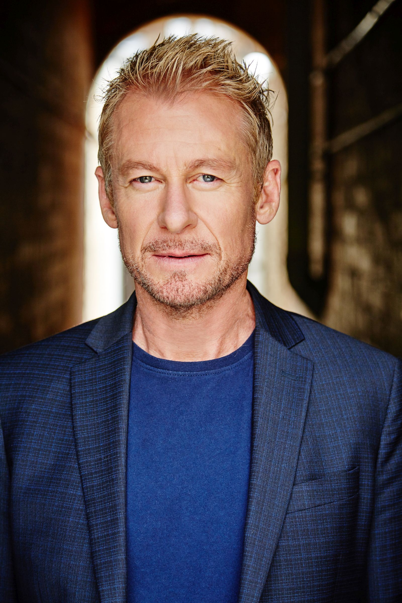 Man with short blond hair wearing a blue blazer and shirt.