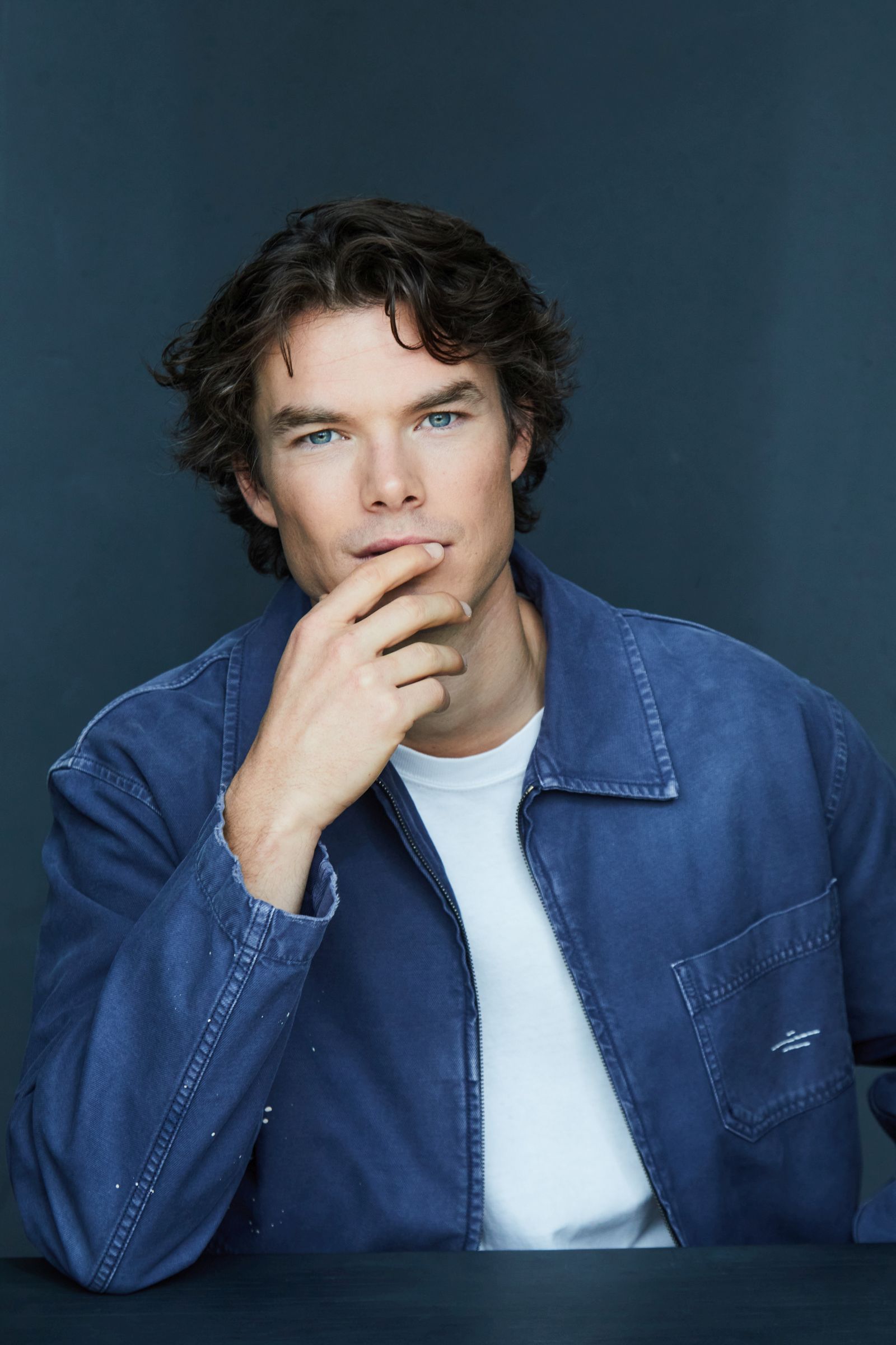 Person in blue jacket posing against a dark blue background.