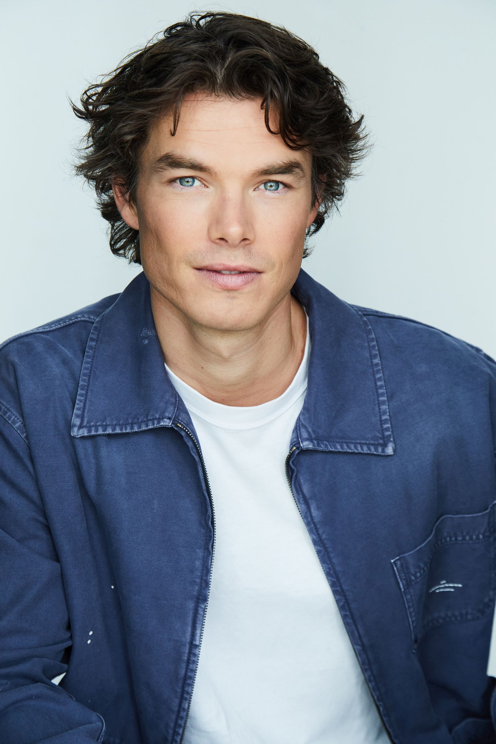 Man with curly hair wearing a blue jacket and white shirt.