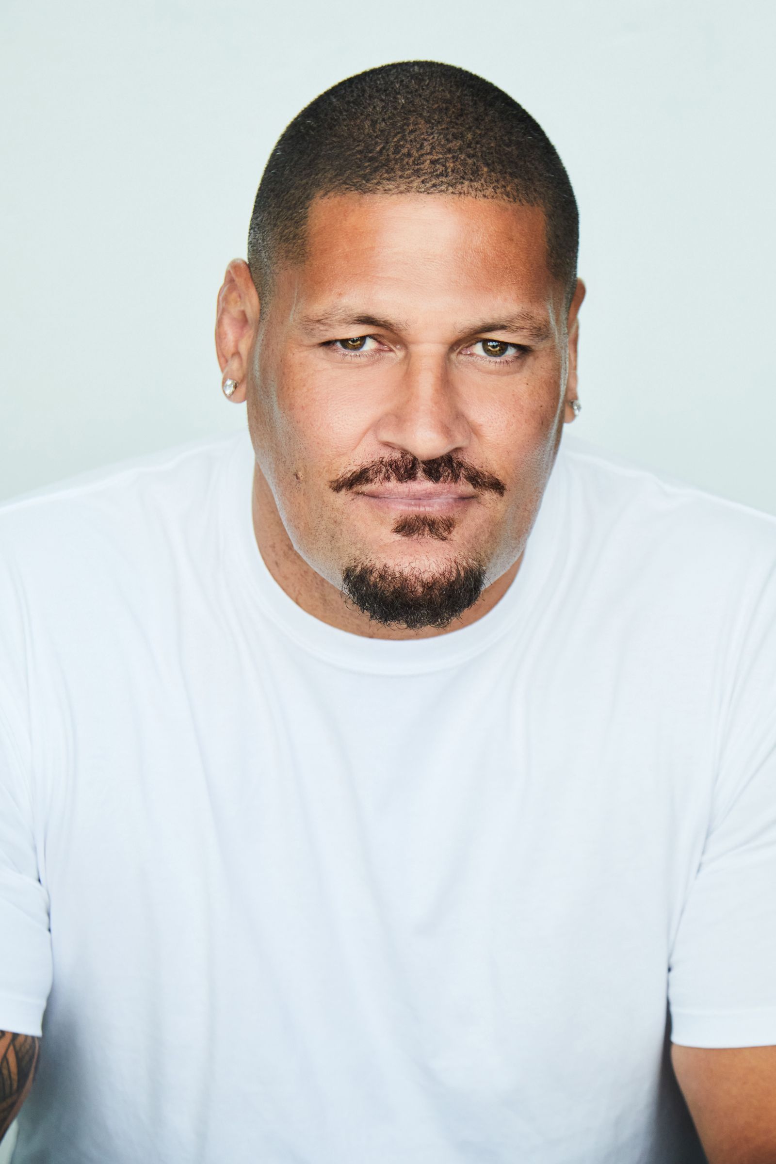 Person with short hair and goatee wearing a white t-shirt, looking at the camera.