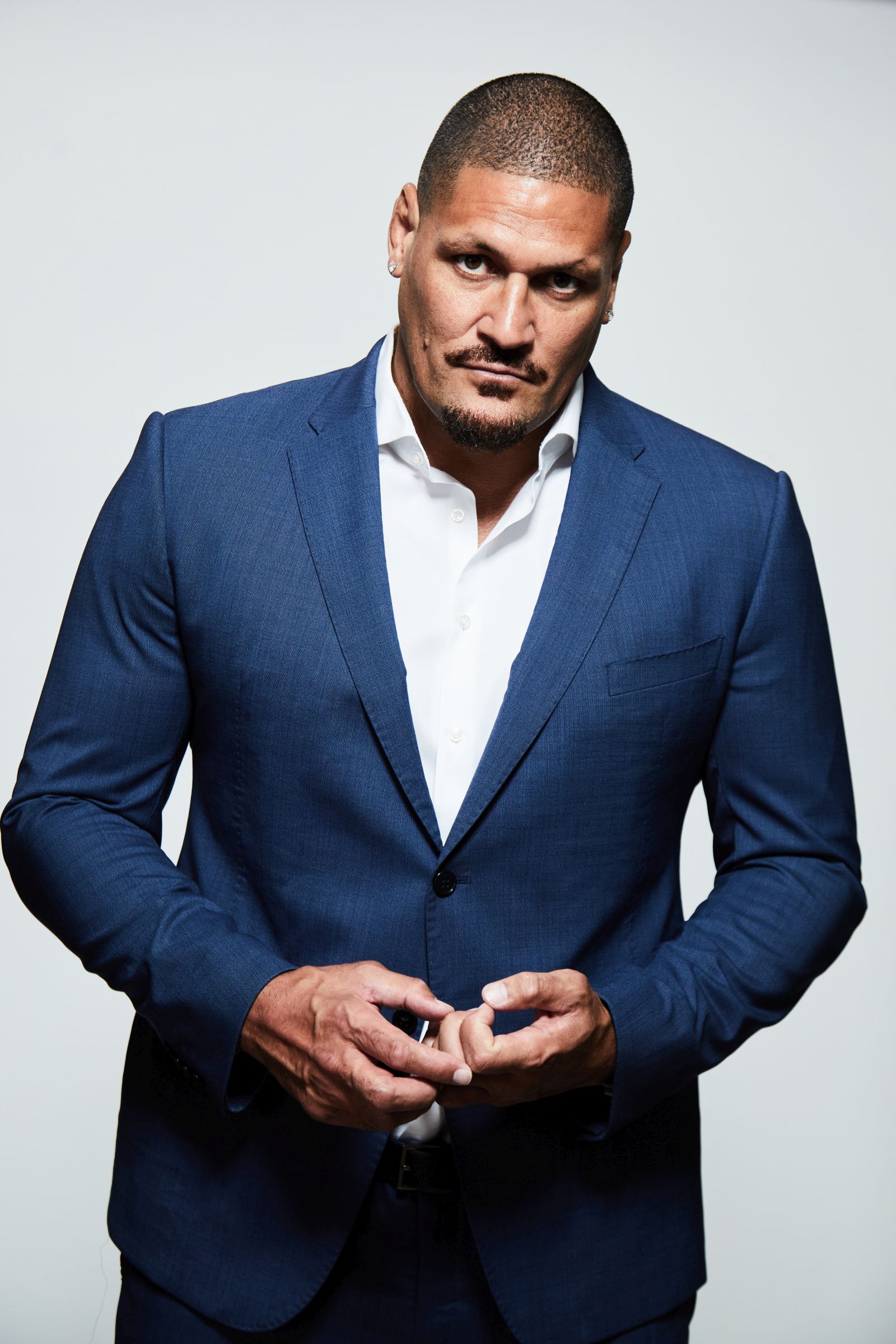 A person in a blue suit with a white shirt against a plain background.