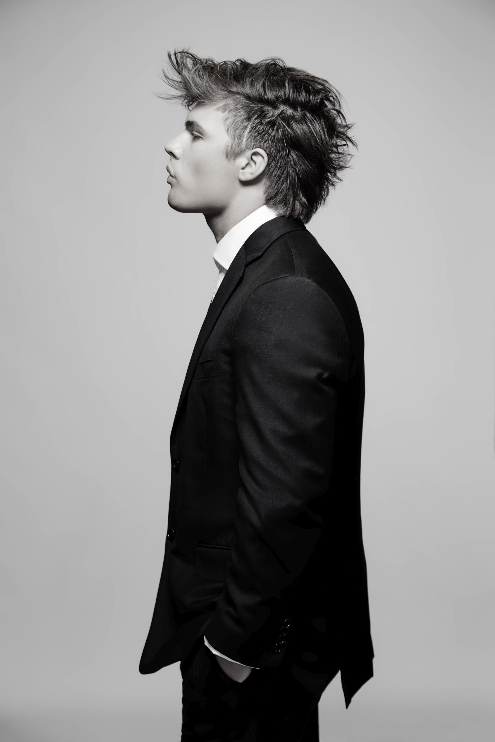 Black-and-white editorial studio portrait, side profile of person in suit, tousled hair.