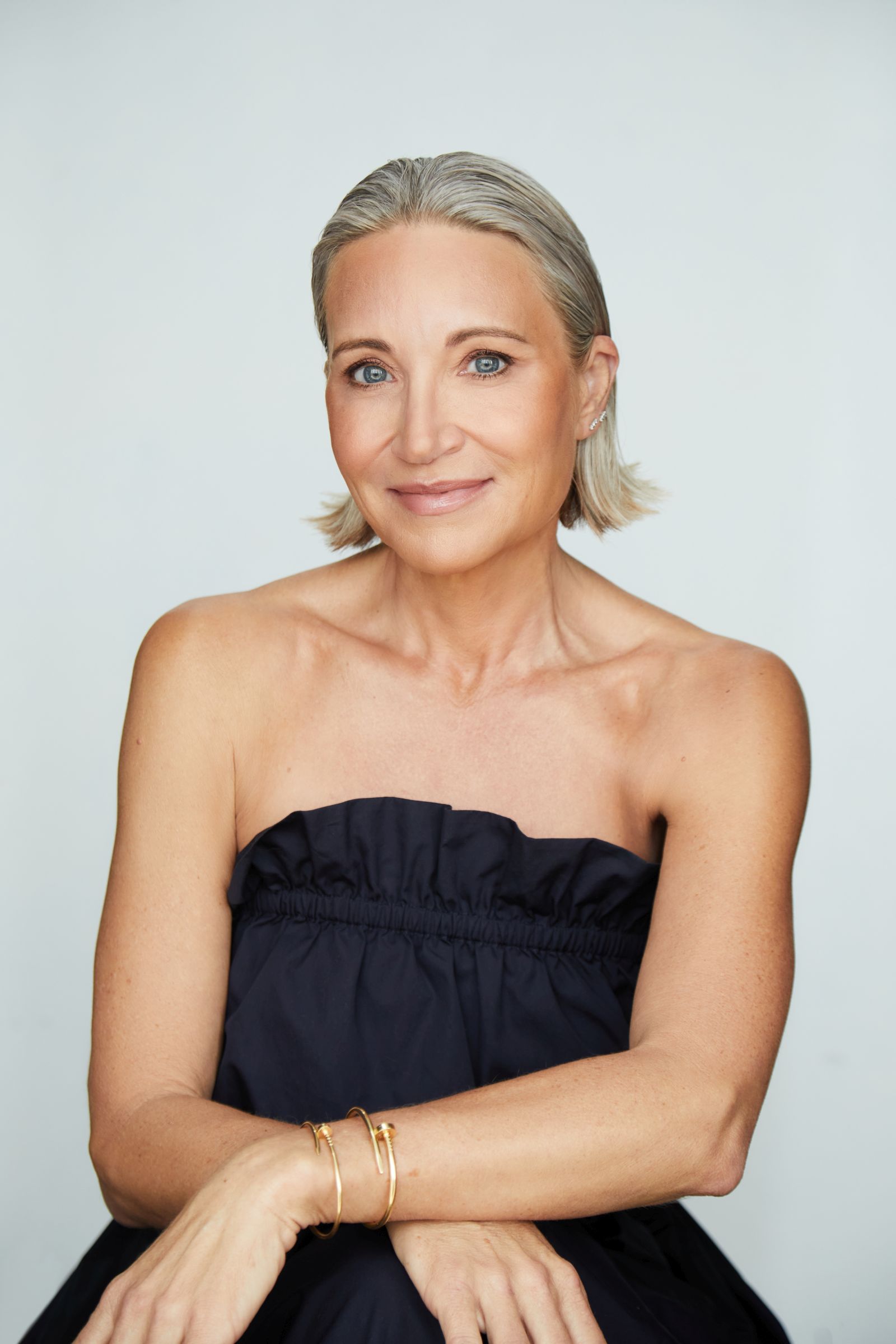 Studio headshot of woman with short silver-blonde hair, black strapless top, gold bangles.
