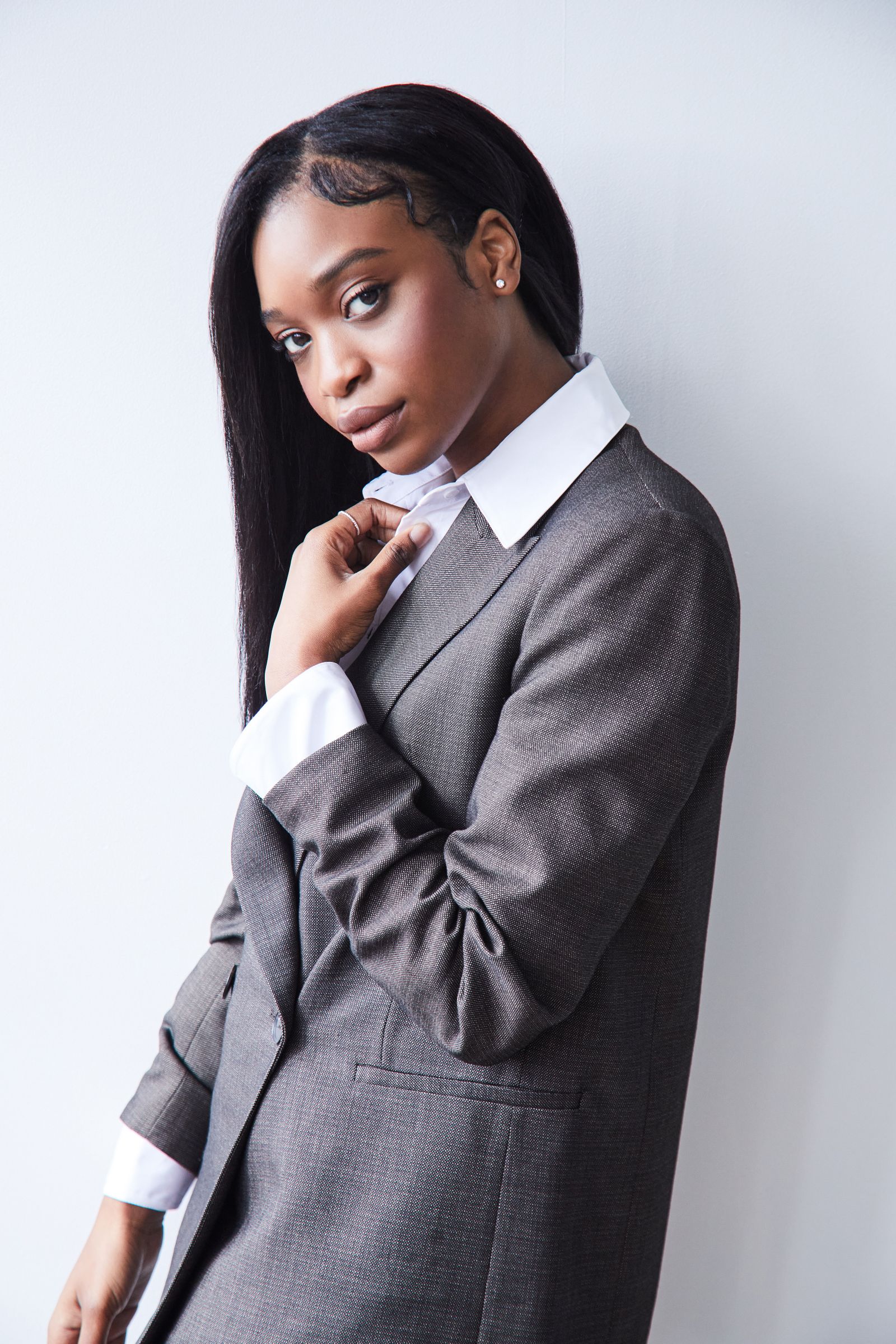 Editorial portrait of person in gray suit adjusting collar, looking at camera.