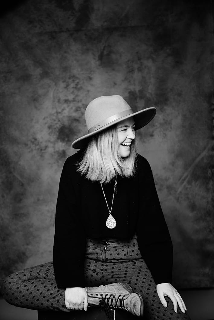 Person wearing a wide-brimmed hat, laughing, and sitting cross-legged.